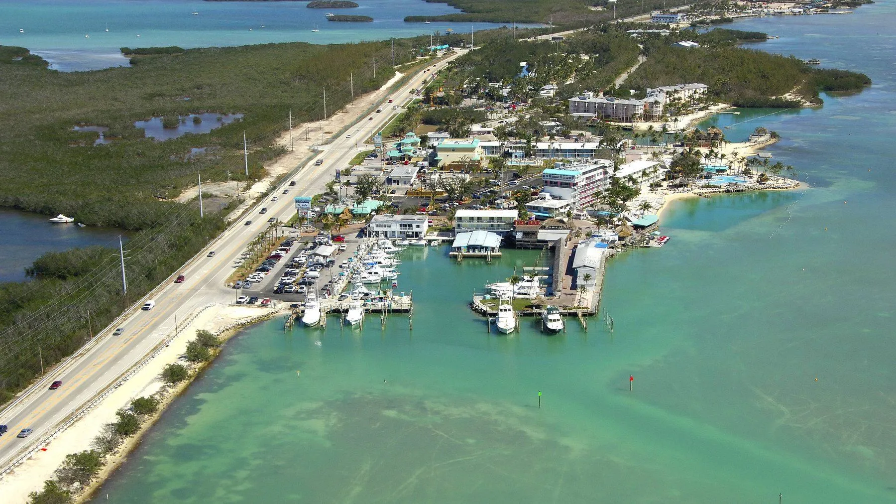 An aerial over Islamorada: the Overseas Highway running between water on both sides, with a marina basin on one and shallow flats on the other